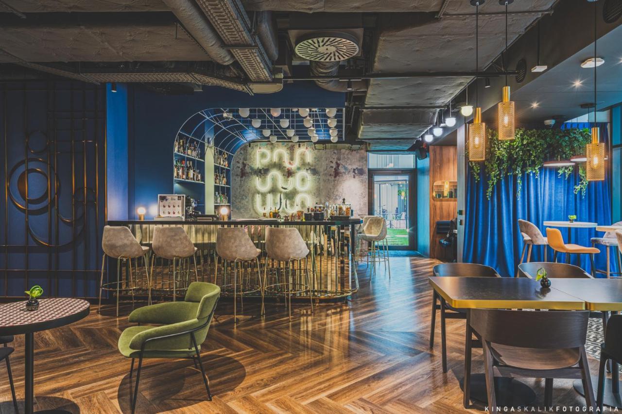 Royal Tulip Warsaw Centre 아파트 호텔 외부 사진 The photo shows a modern and stylish bar or lounge area. It features a curved, elegant bar with high stools arranged in front. Behind the bar, there is a wall with mixed materials, partially illuminated, which likely showcases a selection of drinks. 