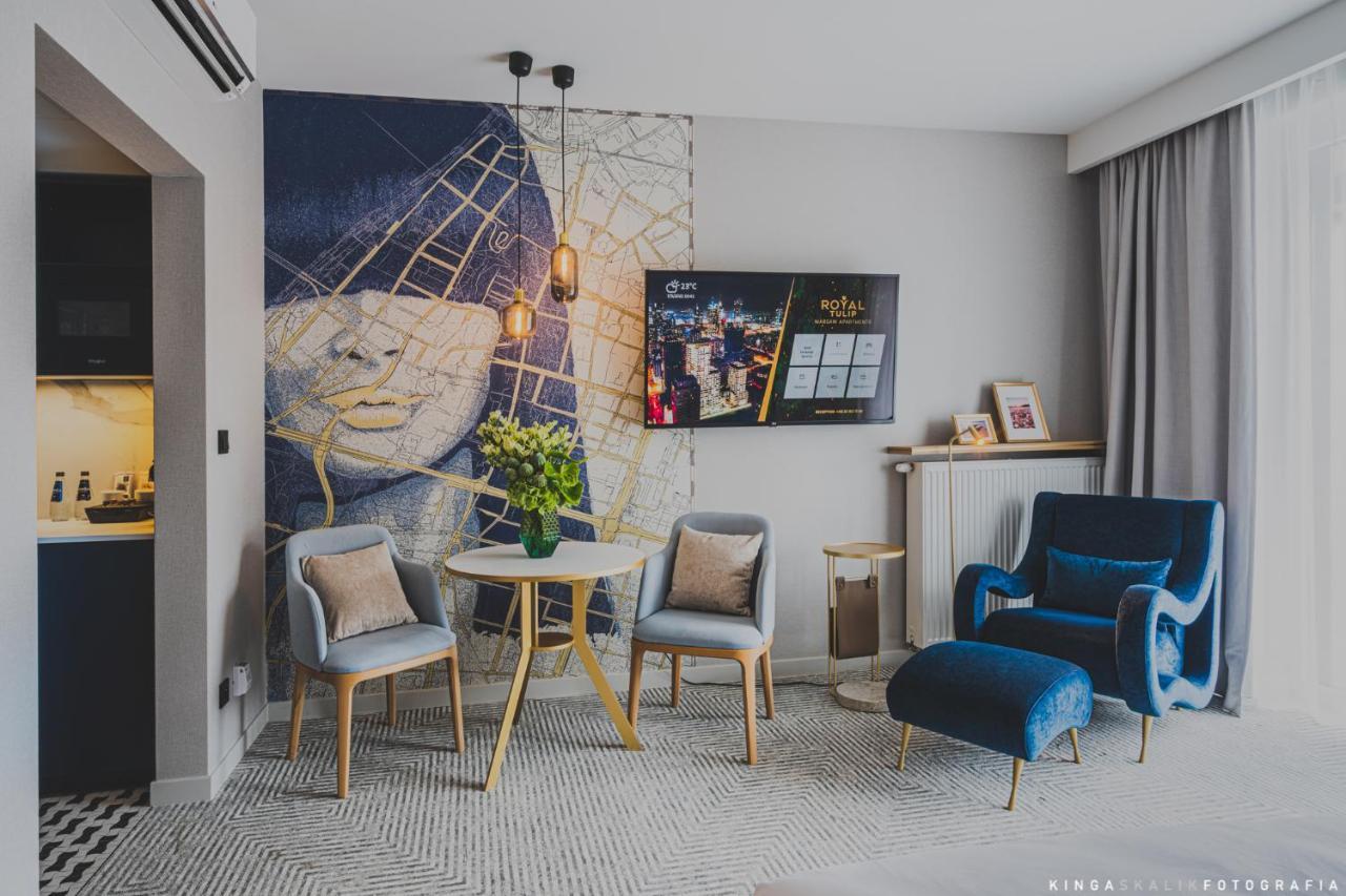 Royal Tulip Warsaw Centre 아파트 호텔 외부 사진 The photo shows a modern living space featuring a stylish interior design. There is a mural on the wall that depicts a face with an abstract background. In the center of the room, there is a small round table surrounded by four chairs. A vase with fl