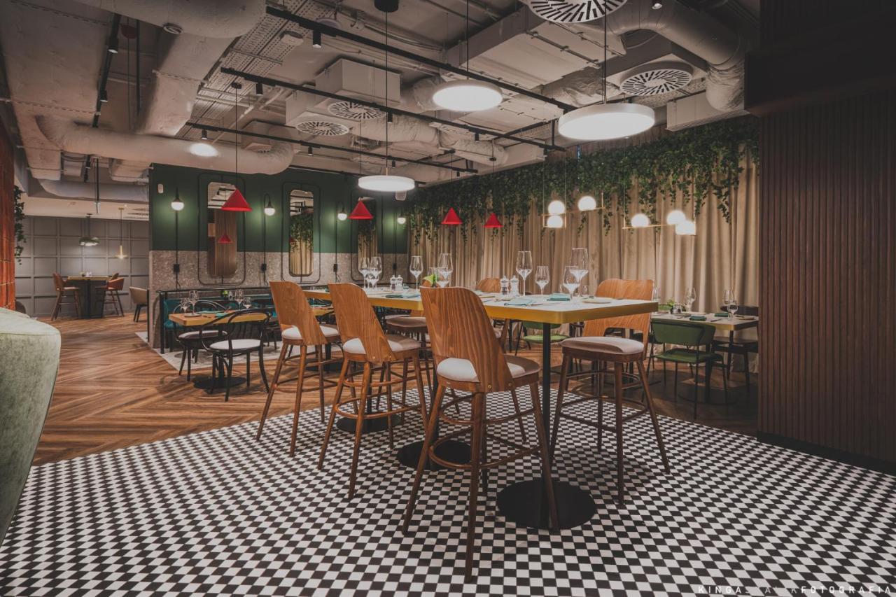 Royal Tulip Warsaw Centre 아파트 호텔 외부 사진 The photo depicts a modern restaurant interior featuring a stylish design. There are high wooden bar stools arranged around a central table. The floor has a black and white checkered pattern, adding a classic touch. The walls are decorated with green