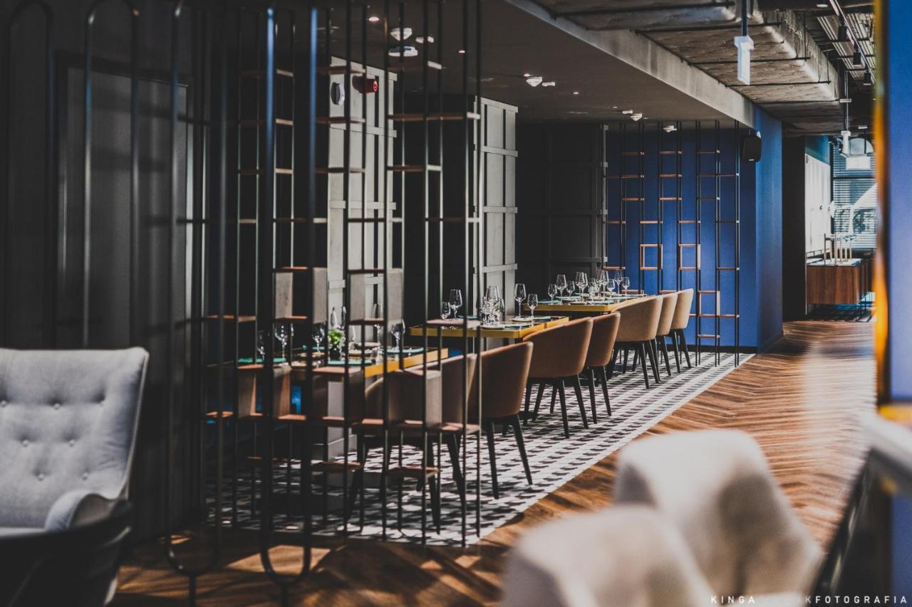 Royal Tulip Warsaw Centre 아파트 호텔 외부 사진 The photo shows a modern restaurant interior. There are multiple dining tables arranged in a long line, each set with tableware and glassware. The space is divided by decorative metal partitions, creating an intimate atmosphere. The flooring features