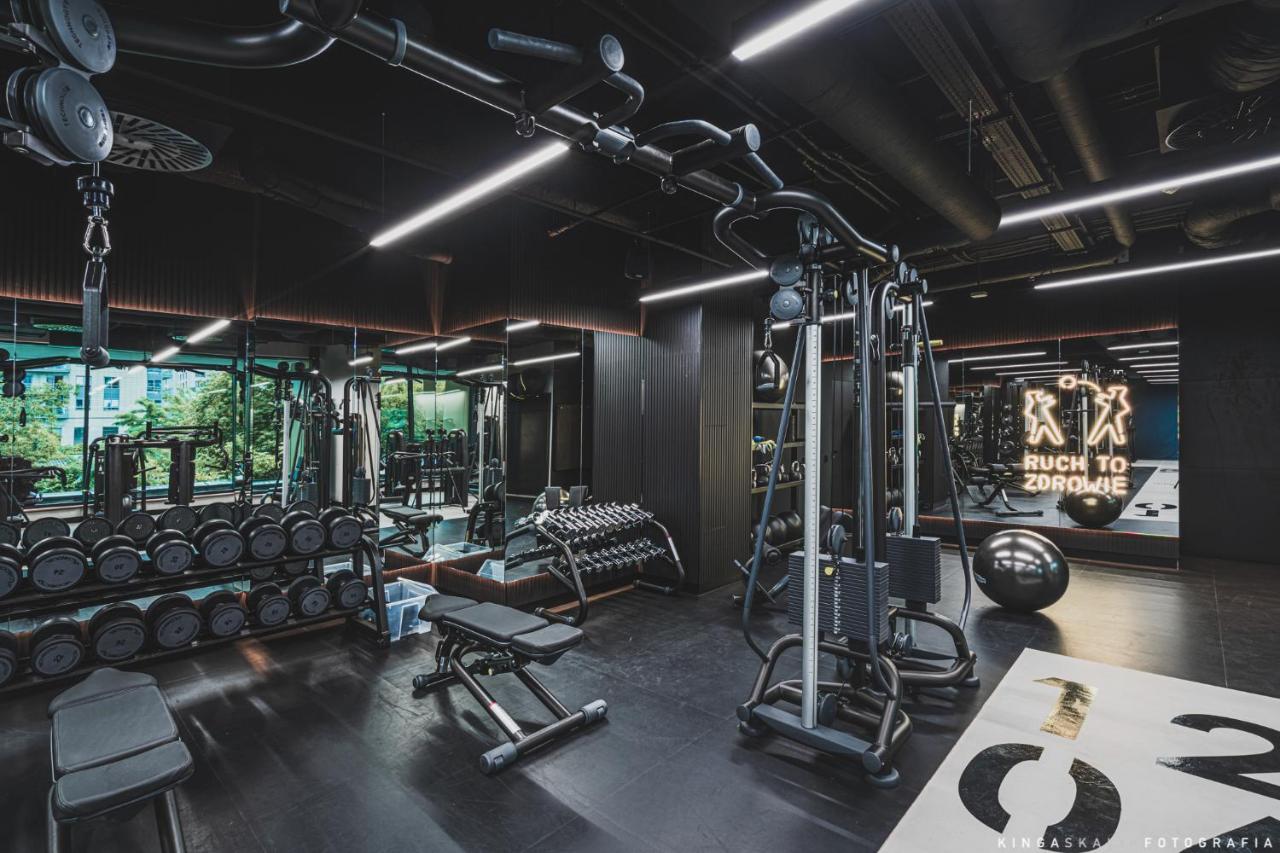 Royal Tulip Warsaw Centre 아파트 호텔 외부 사진 The photo shows a modern gym interior. It features various fitness equipment including a multi-station machine for weight training, benches, and dumbbells. The space has a sleek design with dark colors and plenty of ambient lighting. In the backgroun