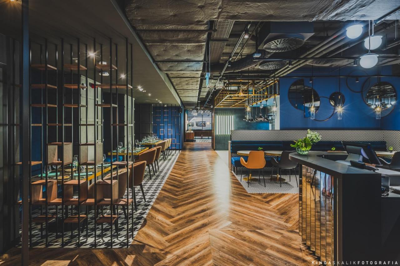 Royal Tulip Warsaw Centre 아파트 호텔 외부 사진 The image shows a modern, stylish restaurant interior. There is a long wooden table with chairs on one side, and a bar area with a shiny counter on the other. The flooring features a herringbone pattern, adding warmth to the space. The walls are pain