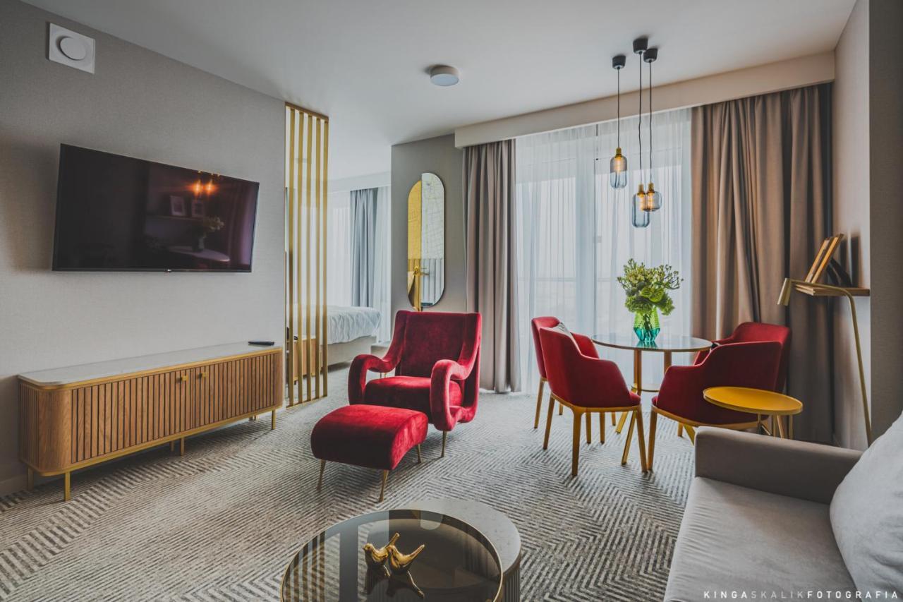 Royal Tulip Warsaw Centre 아파트 호텔 외부 사진 The photo shows a modern and stylish living space. It features a comfortable seating area with a pair of red armchairs and a small round dining table accompanied by two red chairs. A gray sofa is also present. There is a flat-screen TV mounted on the