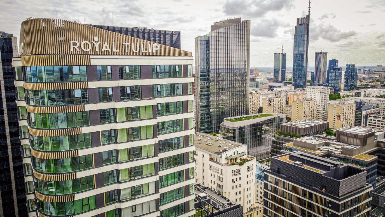 Royal Tulip Warsaw Centre 아파트 호텔 외부 사진 The photo shows a cityscape featuring several modern skyscrapers and buildings. Prominently displayed in the foreground is the "Royal Tulip" hotel, characterized by its contemporary architectural design with large windows. Surrounding it are other ta