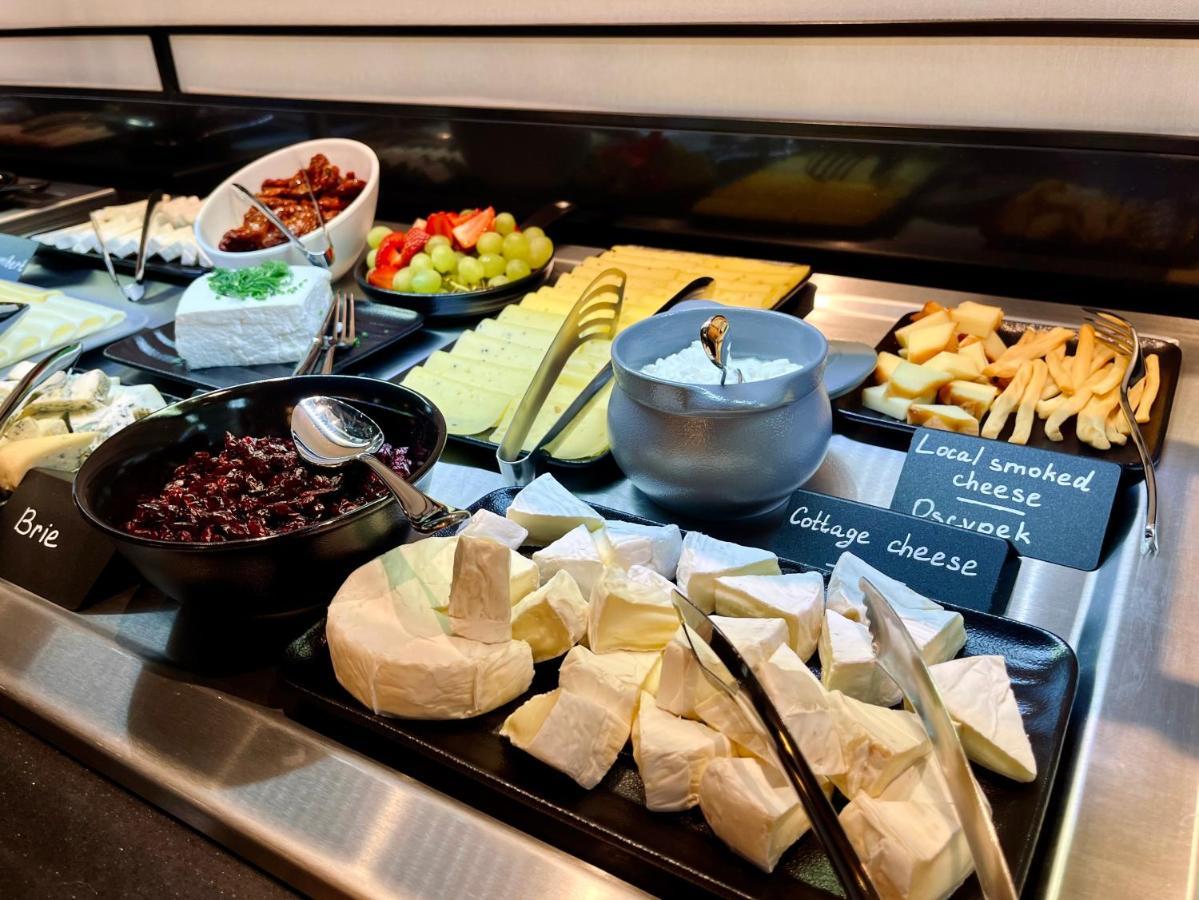 Royal Tulip Warsaw Centre 아파트 호텔 외부 사진 The photo shows a variety of cheeses and accompaniments arranged on a buffet display. There are several types of cheese, including Brie and a soft cheese that appears to be cottage cheese. There's also a bowl of dark-colored cheese, likely a spread. 