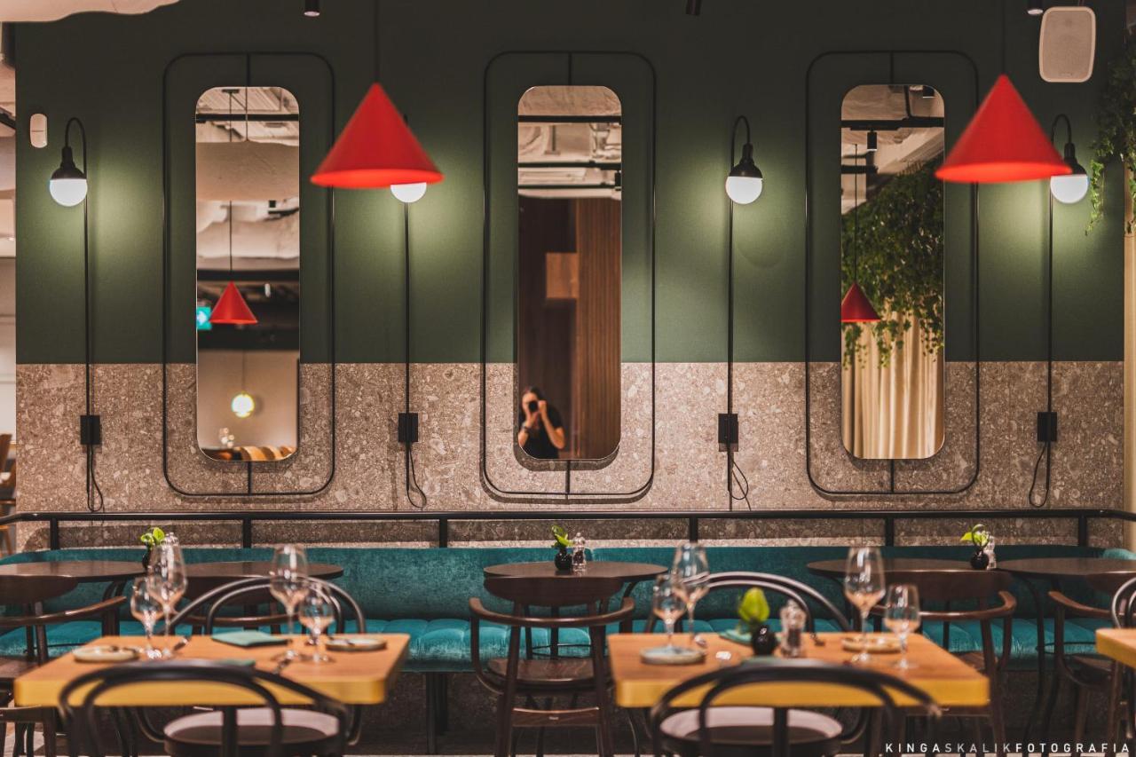 Royal Tulip Warsaw Centre 아파트 호텔 외부 사진 The photo depicts a modern restaurant interior characterized by a stylish design. The walls are painted in dark green, featuring several mirrors set in unique frames. Bright red pendant lights hang from the ceiling, adding a pop of color to the space