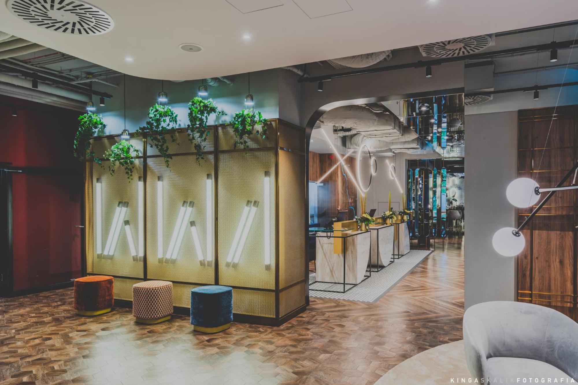 Royal Tulip Warsaw Centre 아파트 호텔 외부 사진 The photo shows a modern interior space, likely a lobby or lounge area. The design features a combination of stylish furniture and decorative elements. There are illuminated wall panels integrated with greenery, creating a fresh aesthetic. In the bac