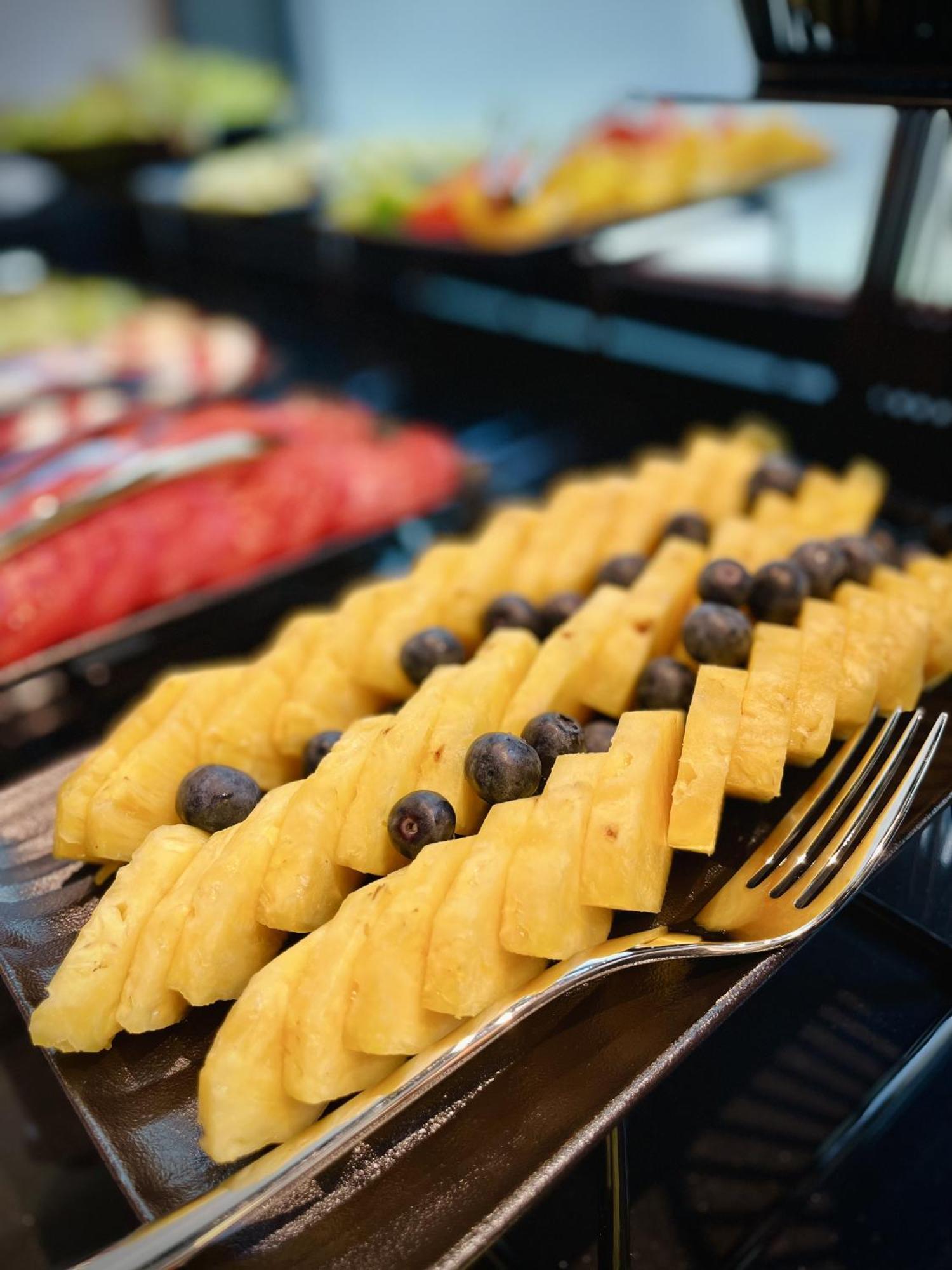 Royal Tulip Warsaw Centre 아파트 호텔 외부 사진 The photo shows a colorful fruit display featuring neatly arranged slices of yellow pineapple, interspersed with dark blueberries. The pineapple slices are cut into a checkerboard pattern, creating an appealing presentation. In the background, other 