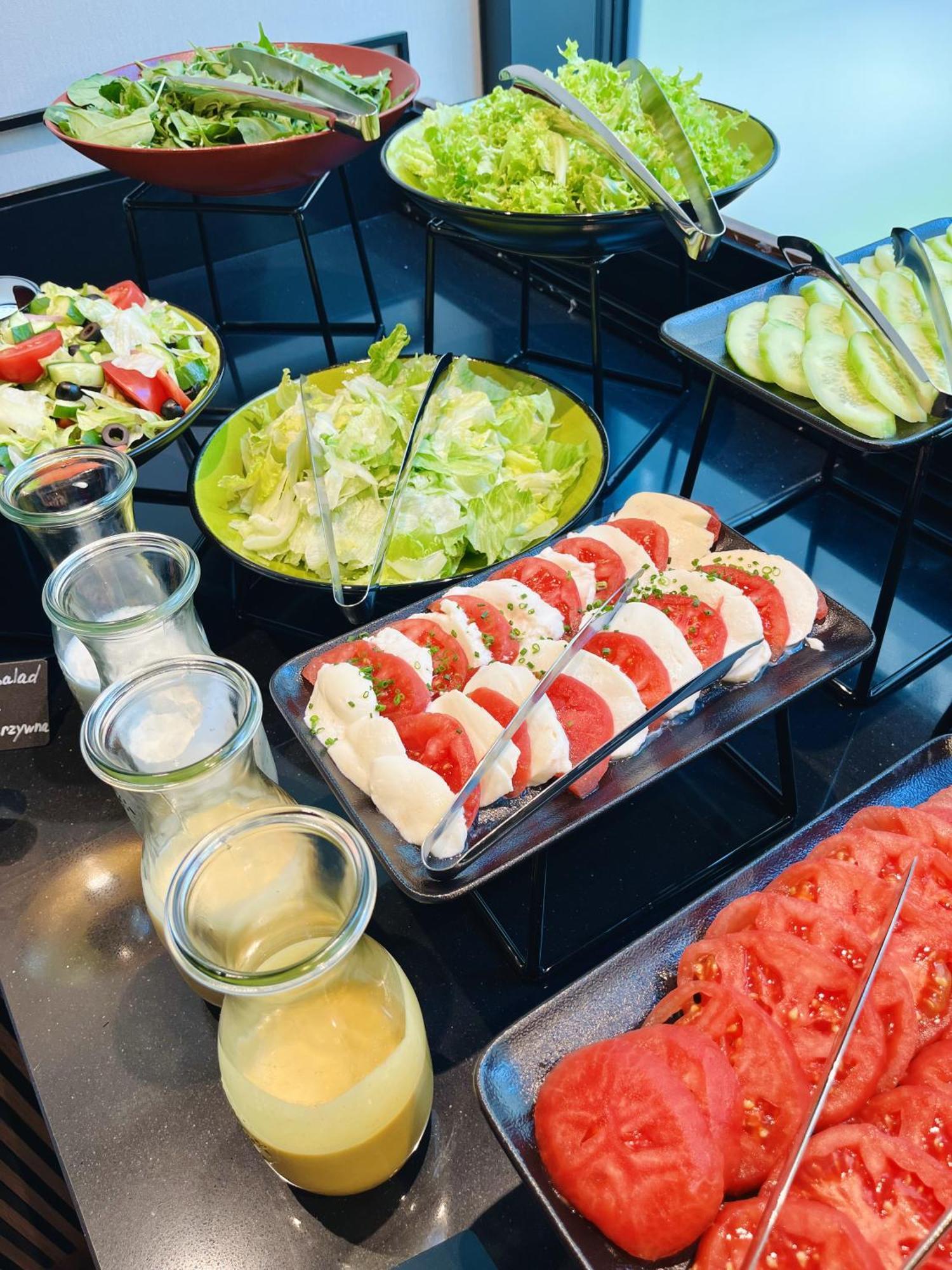 Royal Tulip Warsaw Centre 아파트 호텔 외부 사진 The photo displays a buffet-style arrangement of various salads and ingredients. Specifically, there is a fresh green salad with lettuce and possibly additional vegetables in a large green bowl. In front, there is a platter featuring slices of mozzar