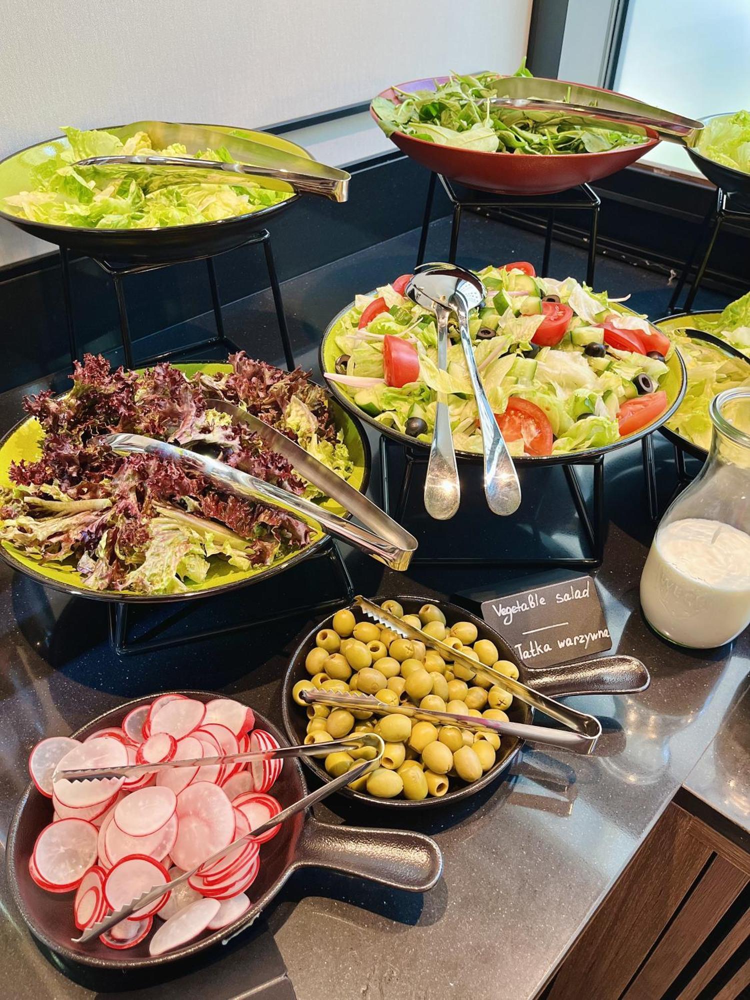 Royal Tulip Warsaw Centre 아파트 호텔 외부 사진 The photo shows a variety of salad options arranged on a table. 

1. **Salads**: There are two larger bowls—one with mixed greens, including red leaf lettuce, and another with a colorful salad that includes chopped tomatoes, cucumbers, and olives.
2.