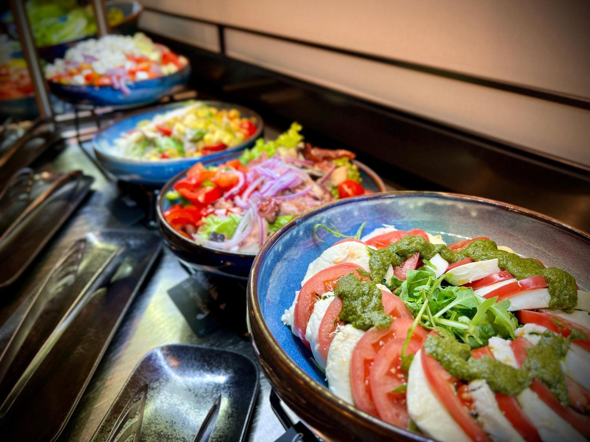 Royal Tulip Warsaw Centre 아파트 호텔 외부 사진 The photo features a variety of dishes arranged in bowls. In the foreground, there is a dish with layers of sliced tomatoes, onions, and a green sauce, likely garnished with herbs or sprouts. In the background, several colorful salads are visible, sh