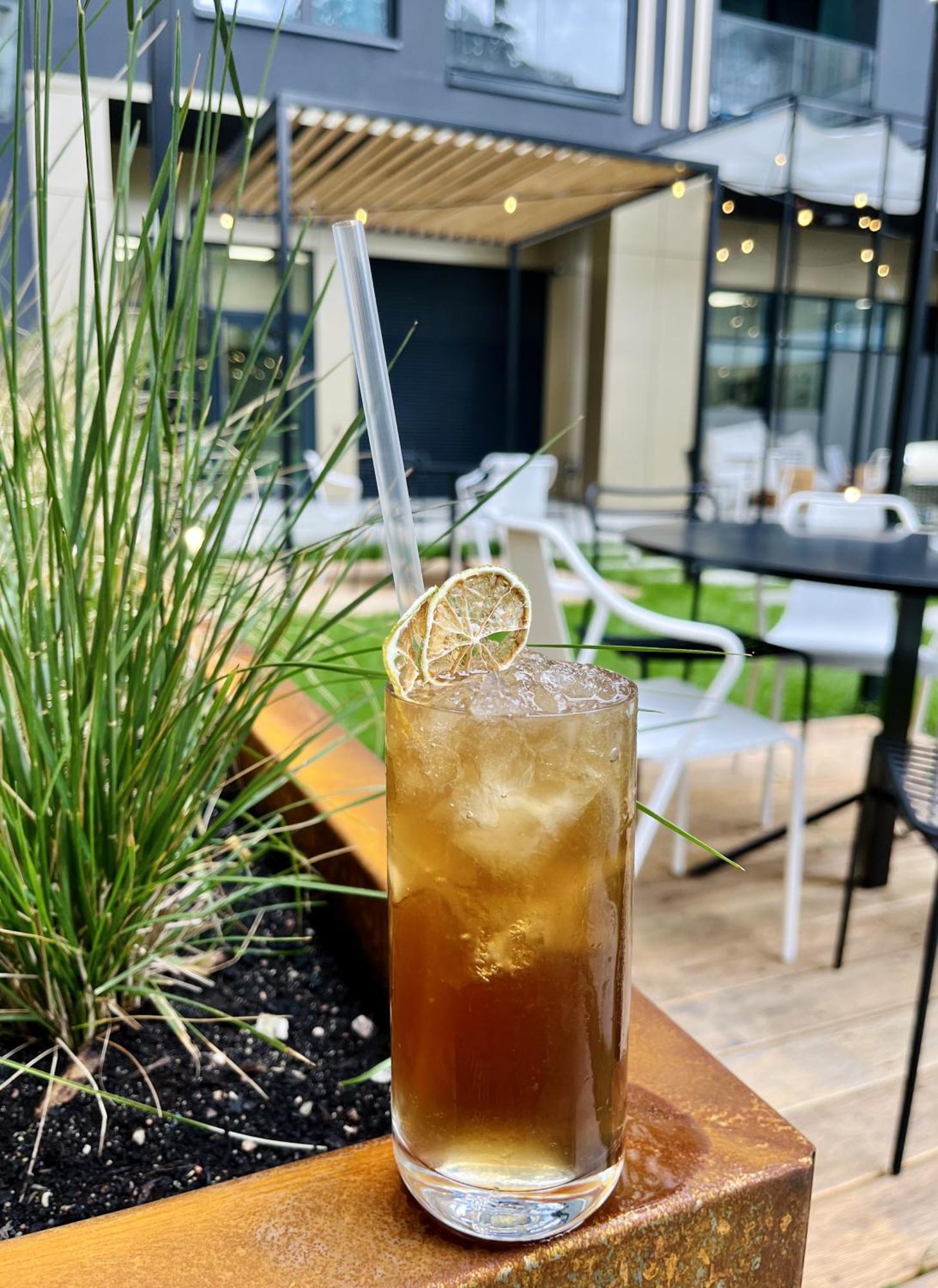 Royal Tulip Warsaw Centre 아파트 호텔 외부 사진 The photo shows a tall glass filled with a dark, fizzy drink, likely a cocktail or a refreshing beverage. It is filled with ice cubes and has a straw for drinking. A slice of dried lime is placed on the rim of the glass, adding a decorative touch. In