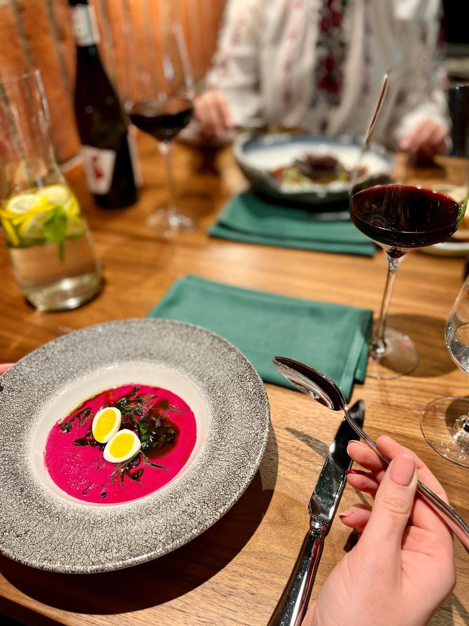 Royal Tulip Warsaw Centre 아파트 호텔 외부 사진 The photo shows a dining table set with multiple dishes and drinks. In the foreground, there is a plate of vibrant pink soup, garnished with small quail eggs and some dark garnish. A hand is holding a spoon, ready to eat. Behind the main dish, there 