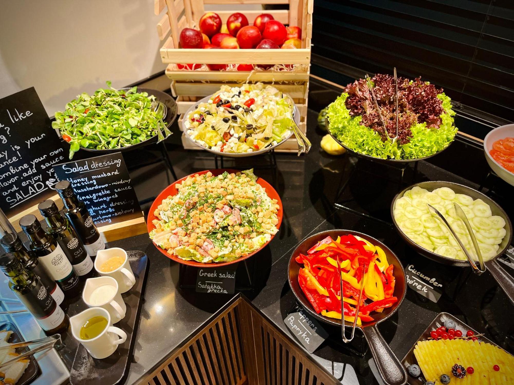 Royal Tulip Warsaw Centre 아파트 호텔 외부 사진 The photo shows a well-arranged salad bar featuring a variety of fresh salads and ingredients. There are several bowls and dishes with different types of salads, including green salads and grain salads. 

1. **Green Salads**: There are multiple bowls